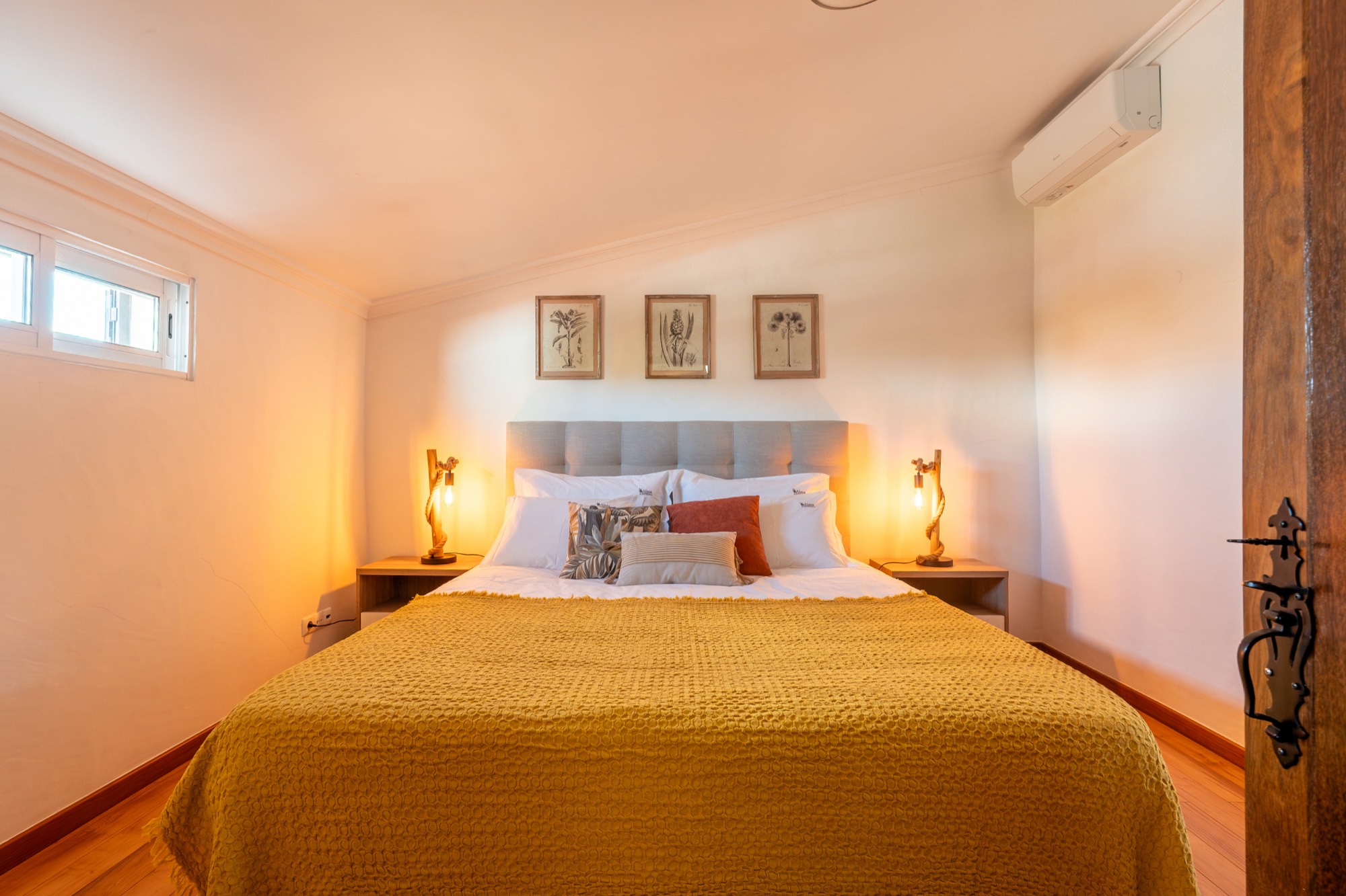 Quarto com cama king size, colcha mostarda e candeeiros de mesa de cabeceira
