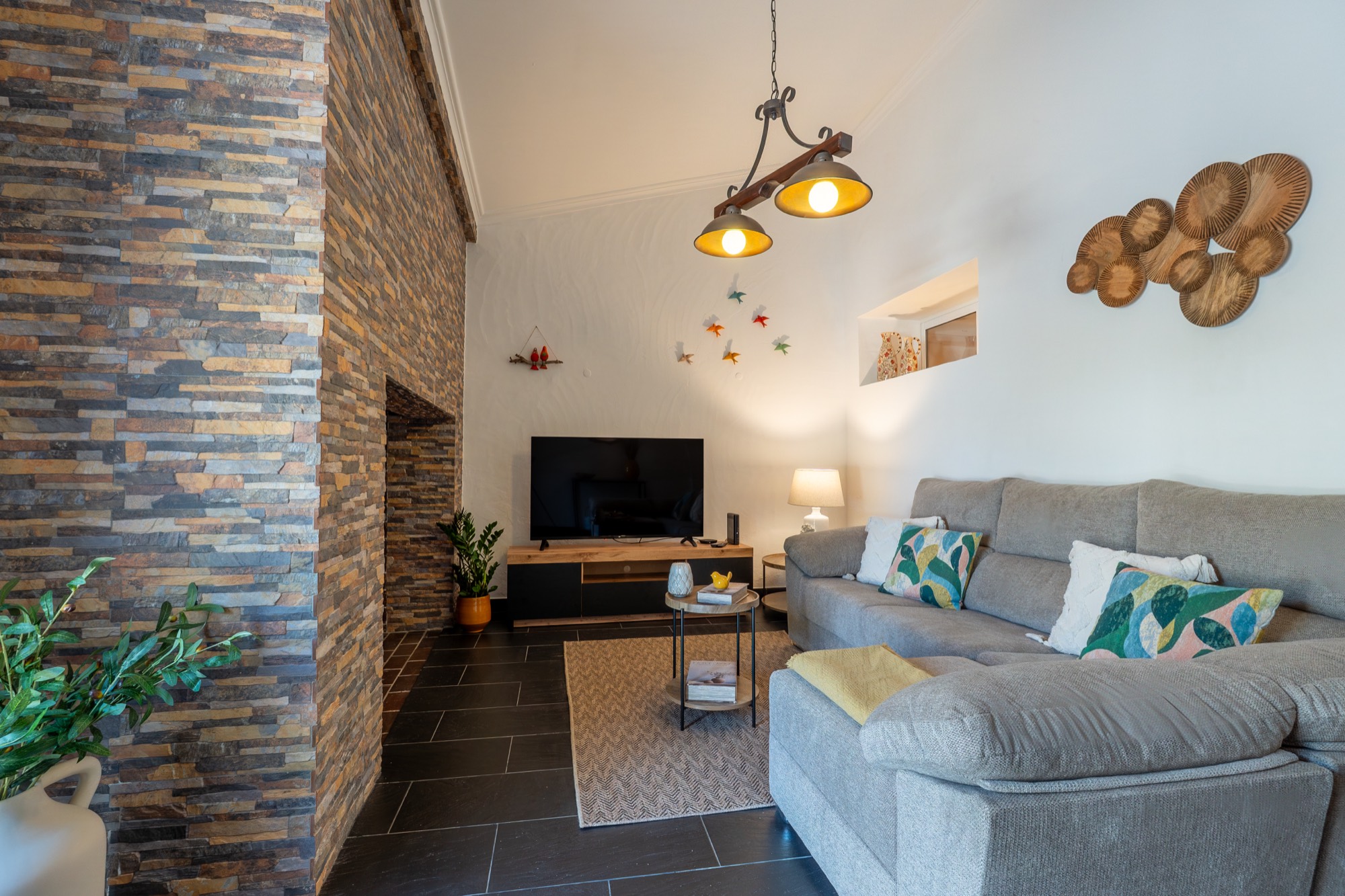 Sala com parede de pedra, lareira, sofá de canto e televisão