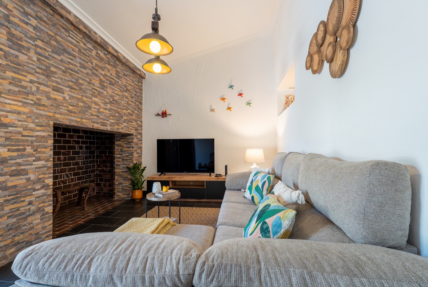 Sala com sofá cinzento, almofadas coloridas e lareira em pedra